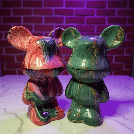 Bear Sculpture Herb GrinderTwo colorful marbled grinder resembling bears on a marble surface with a brick wall background.