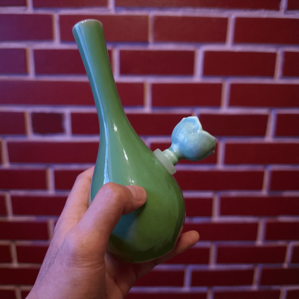 Classic Green Celadon Porcelain Bong with Slim Neck DesignGreen ceramic bong with ceramic bowl is held by hand against a brick wall background