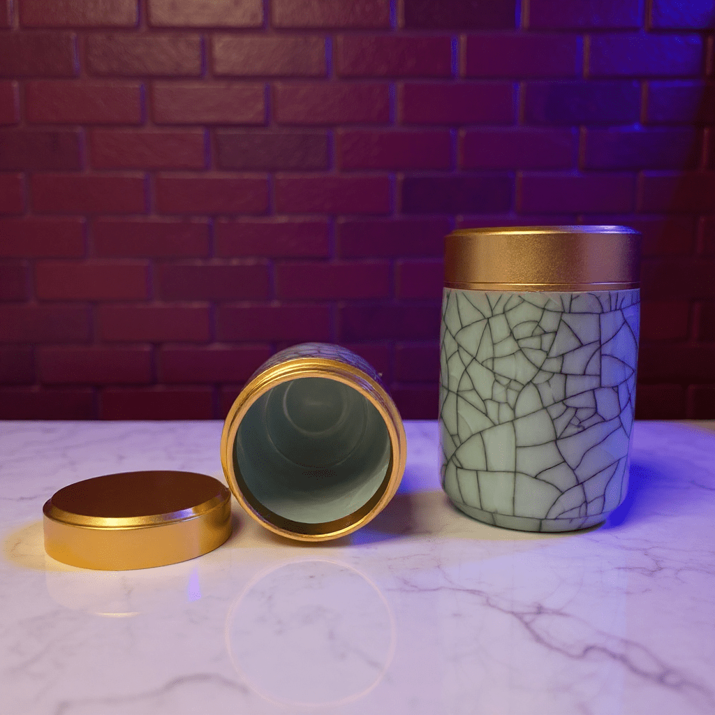 Crackled Blue - Green Celadon Porcelain Stash JarTwo celadon porcelain containers with gold lids on a marble surface against a brick wall.