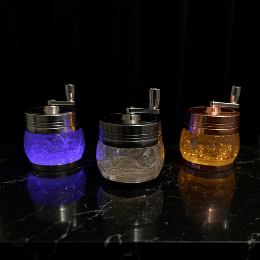 Crystal Hand Crank Herb Grinder - Three designer grinders in purple, bronze, and amber displayed on a bed.