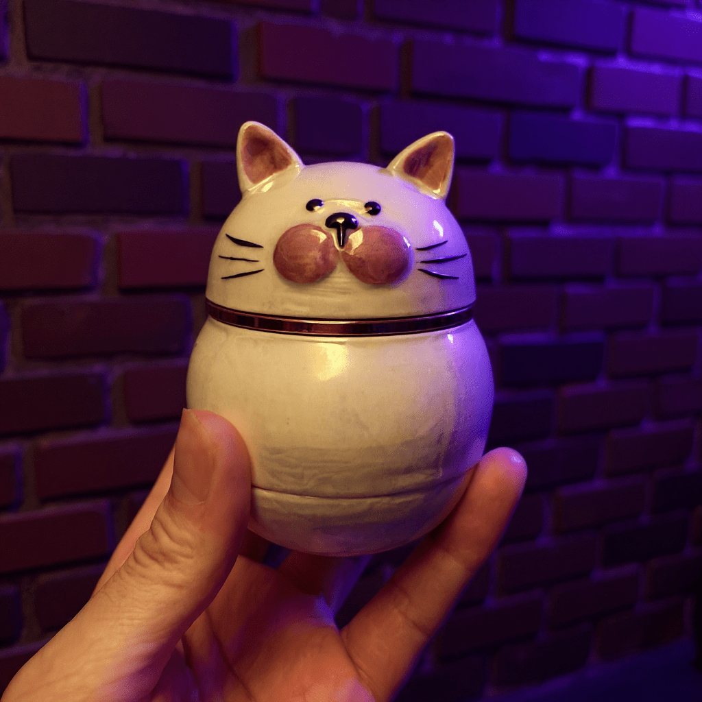 Cute Ceramic Cat Herb Grinder – Spice CrusherCeramic cat - shaped grinder held in front of a brick wall with purple lighting