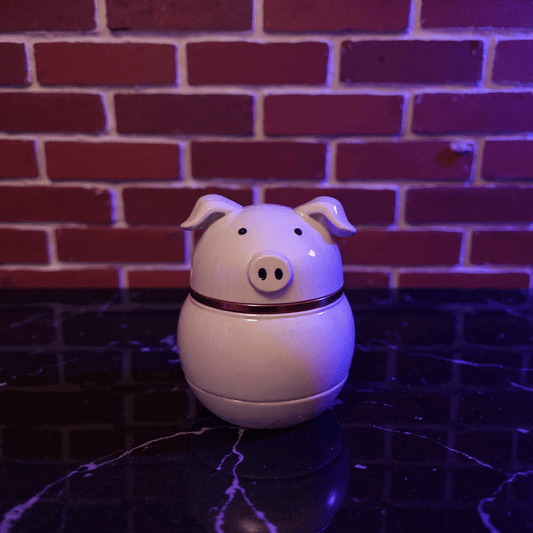 Cute Pig Ceramic Herb Grinder – Spice Crusher- White pig shaped ceramic grinder on a dark surface with a brick wall