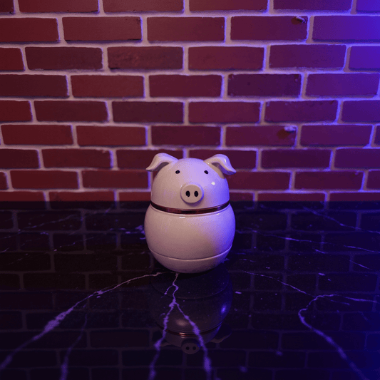 Cute Pig Ceramic Herb Grinder – Spice CrusherWhite pig - shaped weed grinder on a dark surface with a brick wall background