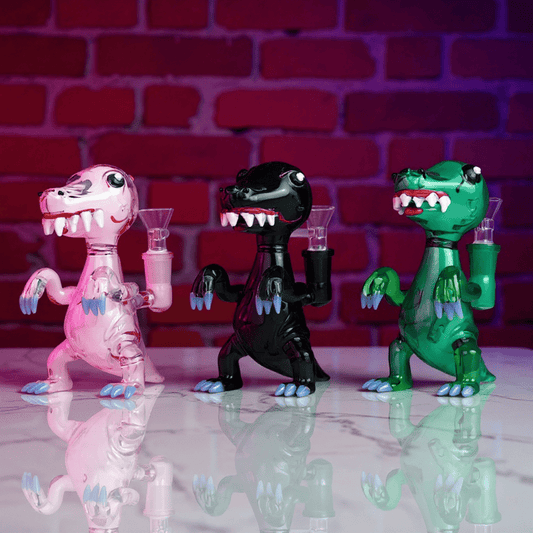 DinoRex Glass Bong - Borosilicate Glass DragonThree colorful dinosaur - like glass bongs with pan against a brick wall background.