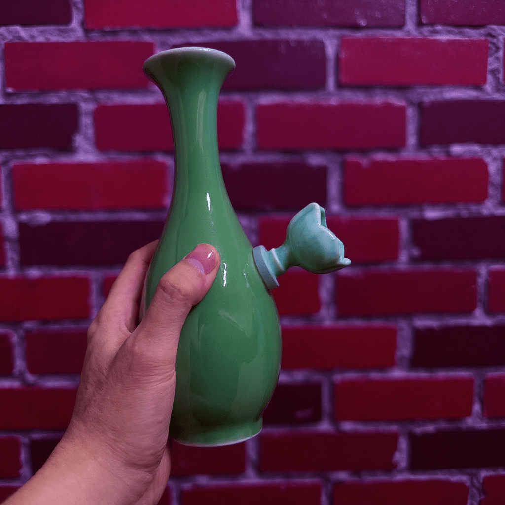 Glossy Green Celadon Bong with Flared TopGreen ceramic bong held against a red brick wall