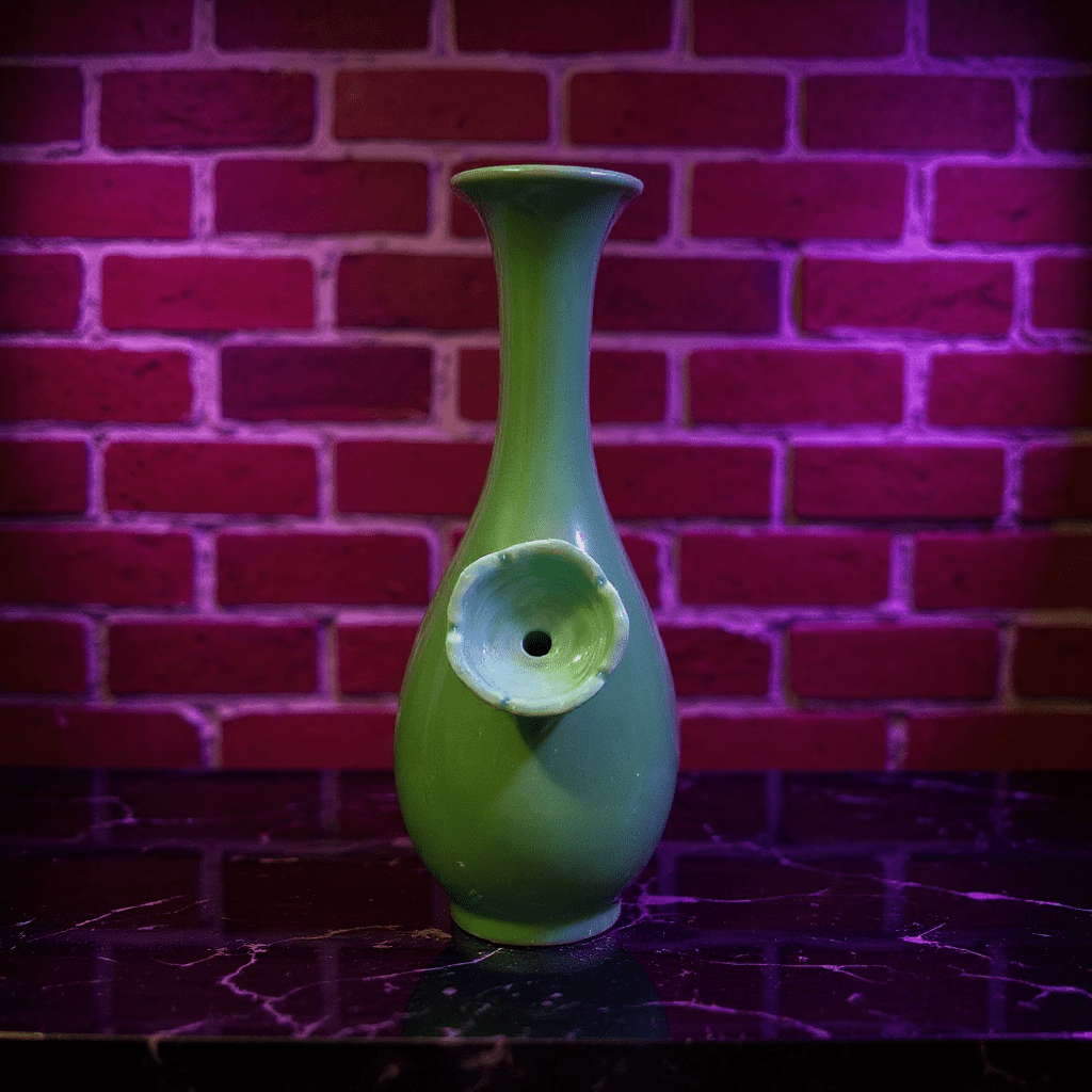 Glossy Green Celadon Bong with Flared TopGreen ceramic bong with a unique design ceramic bowl against a brick wall background
