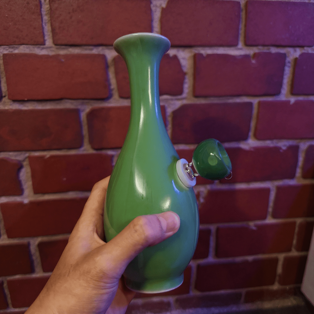 Glossy Green Celadon Bong with Flared TopGreen ceramic bong held in front of a brick wall