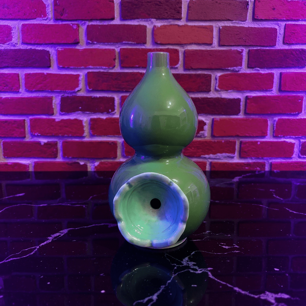 Glossy Green Celadon Gourd Porcelain BongGreen ceramic gourd - shaped bong on a dark surface with a brick wall background