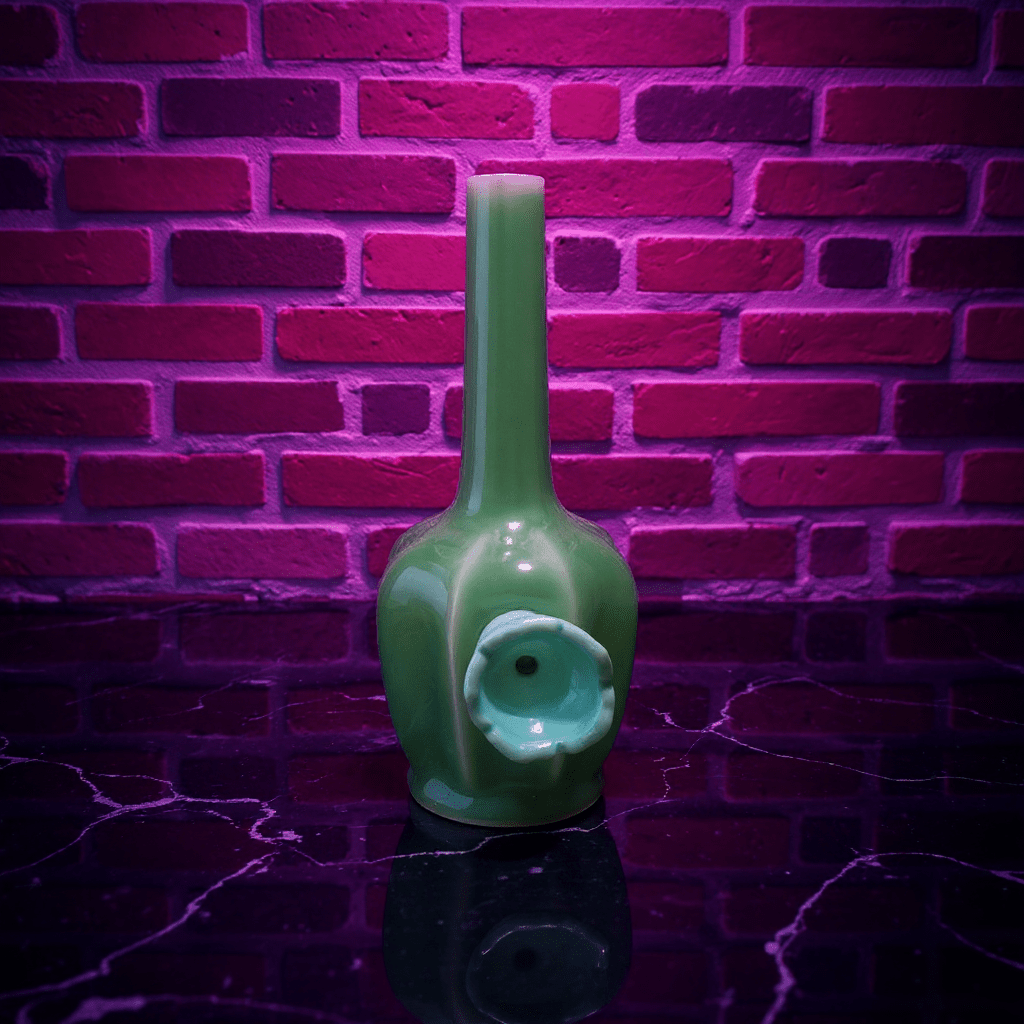 Glossy Green Flat - Sided Celadon Porcelain BongGreen ceramic bong with decorative elements against a brick wall.