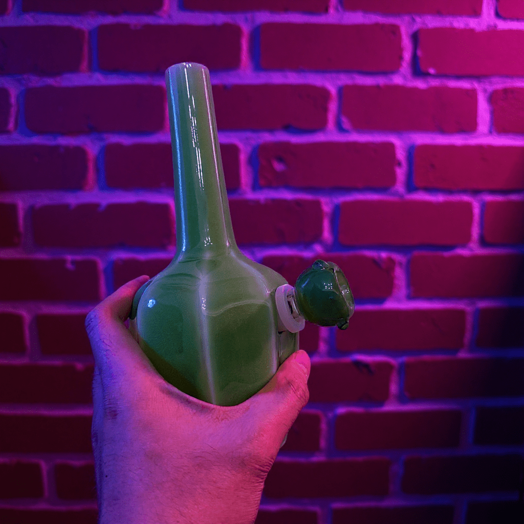 Glossy Green Flat - Sided Celadon Porcelain BongGreen ceramic pipe held against a brick wall with purple lighting