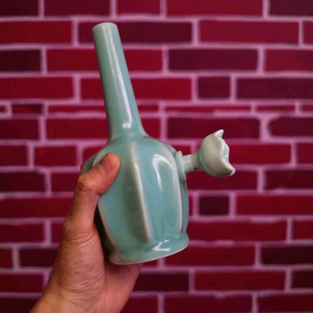 Glossy Light Blue Celadon Flat - Sided Porcelain Bongblue ceramic bong held against a red brick wall