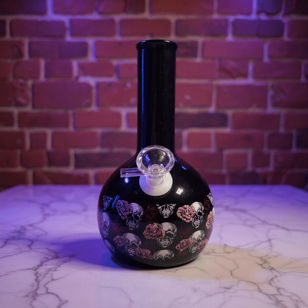 Gothic Skull Rose Ceramic Bong – Black ceramic bong with colorful designs on a marble surface against a brick wall.