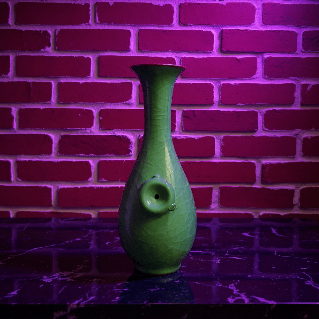 Green Ice - Crack Celadon Porcelain Bong with Flared TopGreen ceramic bong against a brick wall with purple lighting