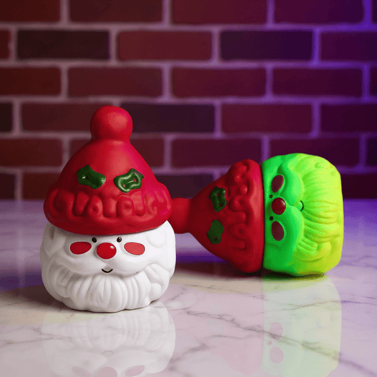 Herb Grinder – Holiday Edition, Two colorful grinders resembling a Santa Claus figure and a caterpillar on a marble