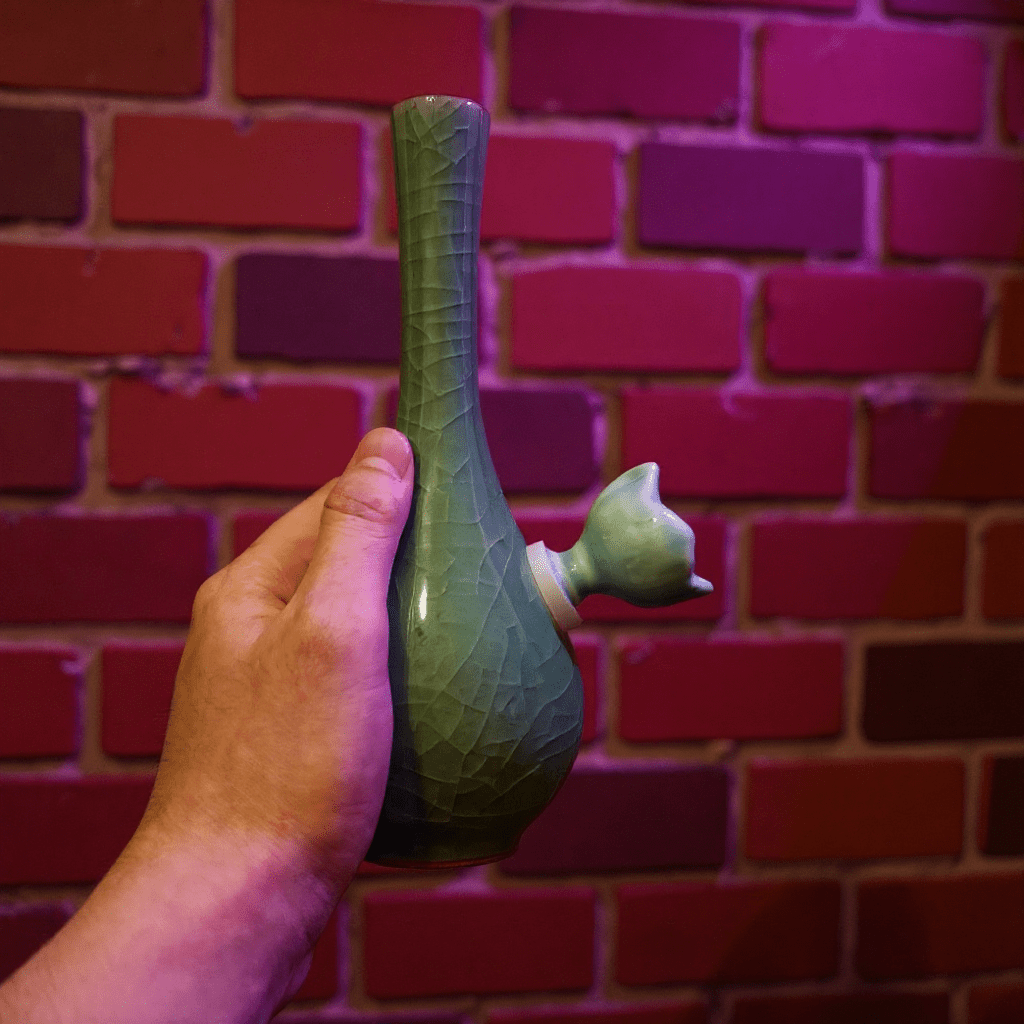 Ice - Crack Celadon Bong with Slim Neck DesignHand holding a green ceramic bong against a brick wall.