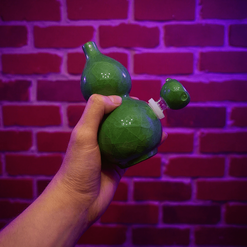 Ice - Crack Green Celadon Gourd Porcelain BongGreen ceramic bong held by a hand against a brick wall with purple lighting