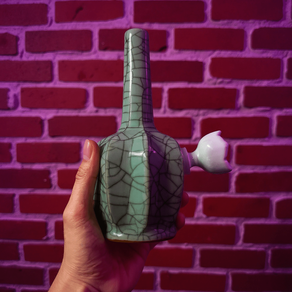 Ice - Crack Light Blue Celadon Flat - Sided Porcelain BongHand holding a ceramic bong with a textured design against a brick wall