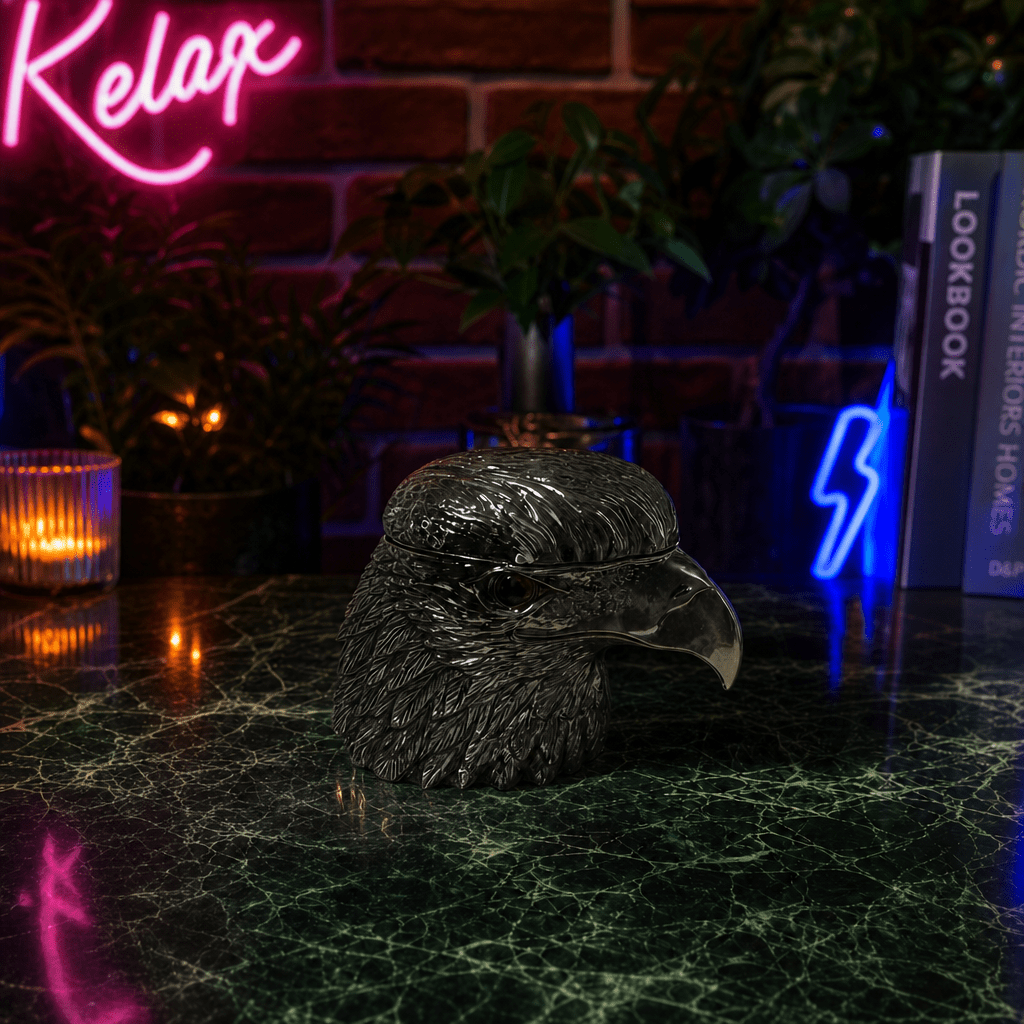 Patriot Eagle Head Metal Grinder – Brass, Bronze & Black FinishDecorative eagle head sculpture on a dark surface with neon signs and plants in the background.