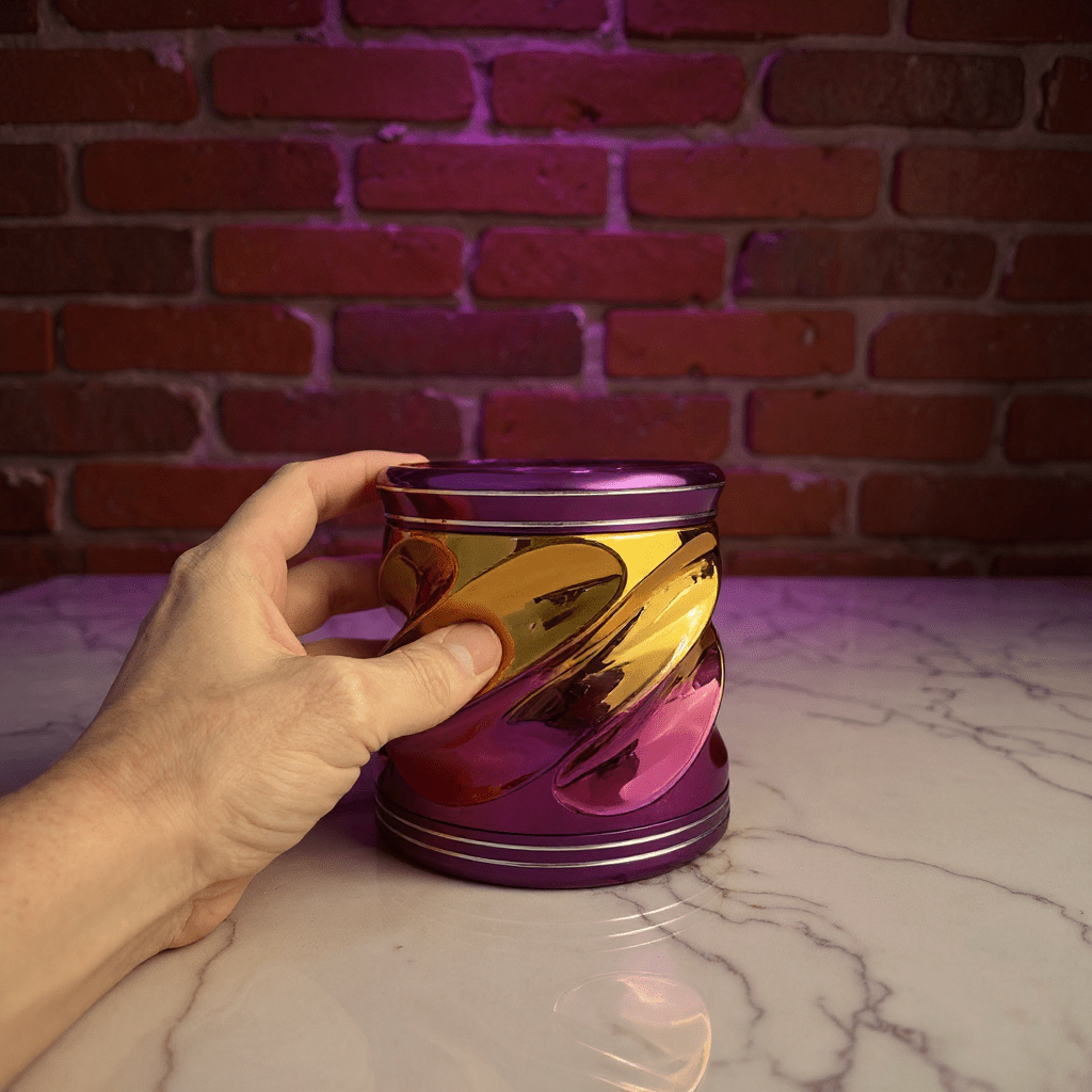 Spiral Grip Aluminum Herb Grinder - Hand holding a reflective purple and gold grinder against a brick wall.