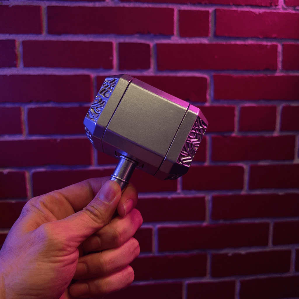 Thor Hammer Shape Grinder – 4 - Part Metal GrinderHand holding a silver hammer grinder against a brick wall