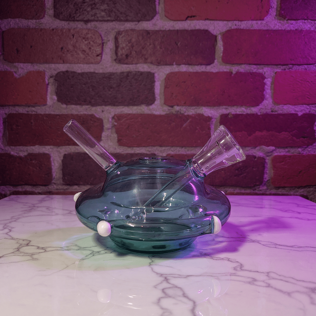 UFO Mini Glass Bong – Water Pipe in 3 ColorsGlass smoking pipe on a marble surface with a brick wall background