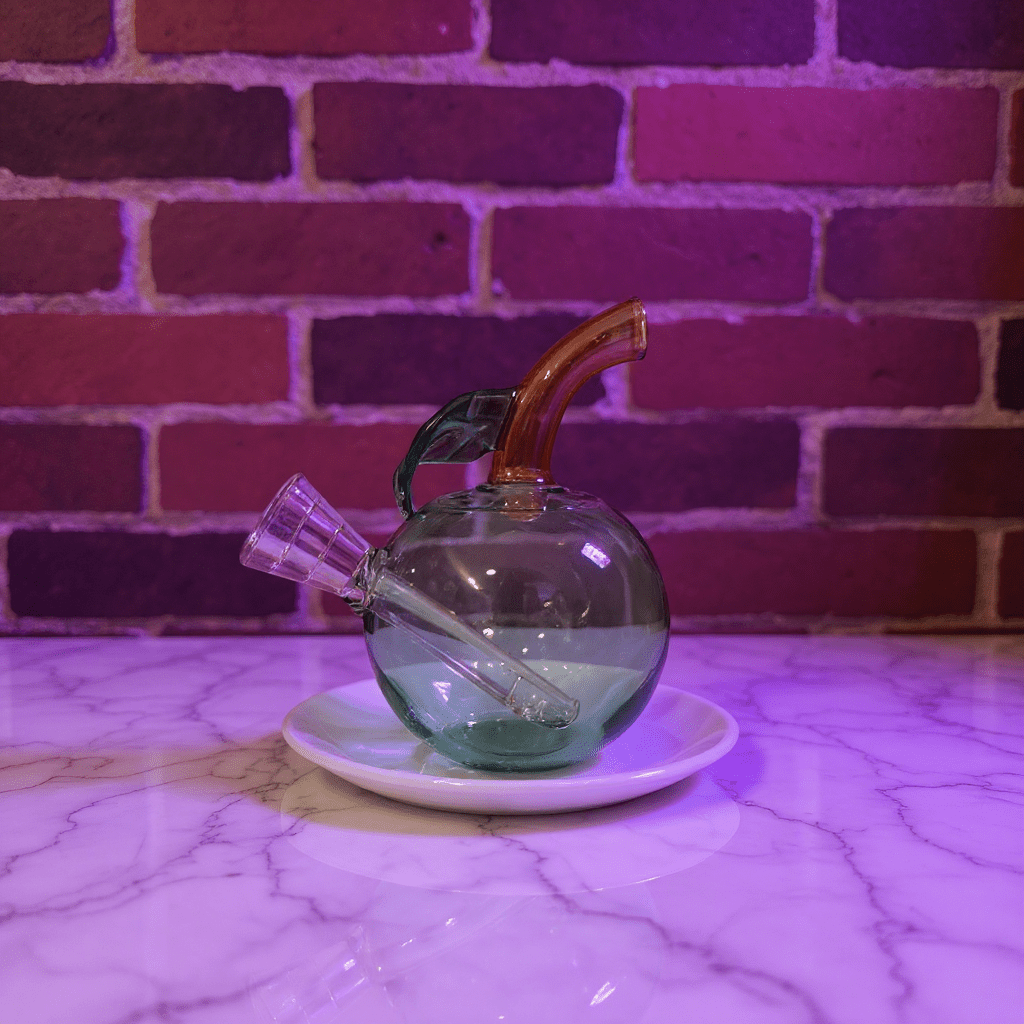 🍎 Apple Glass Bong – Mini Fruit Water PipeGreen glass smoking bong on a white plate with a brick wall background