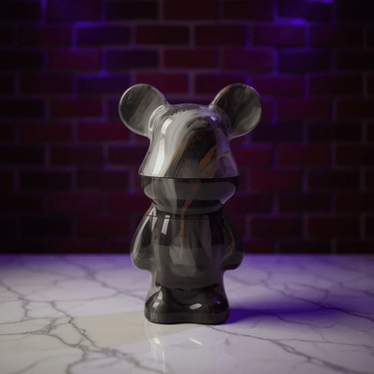Bear Sculpture Herb Grinder - Black mouse - shaped herb grinder on a marble surface with a brick wall background
