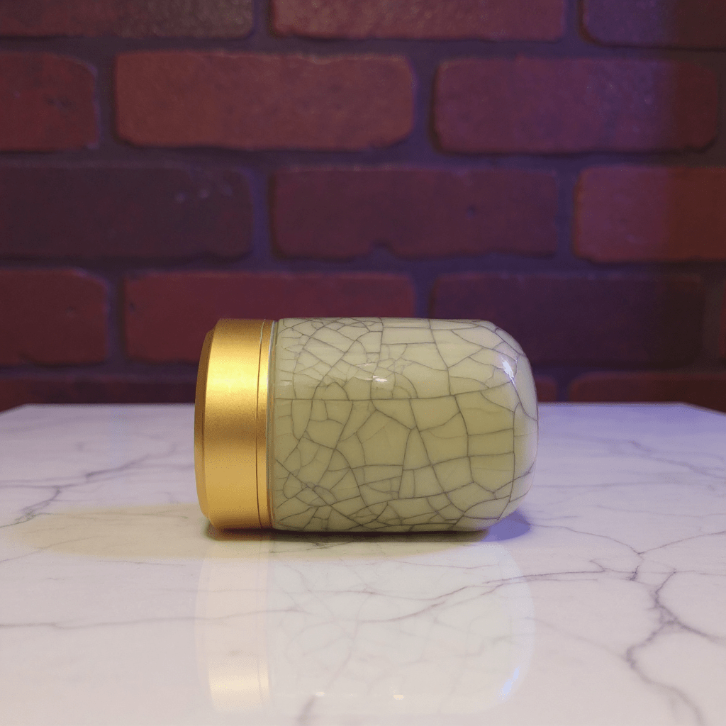 beige celadon porcelain container with gold lid on a marble surface