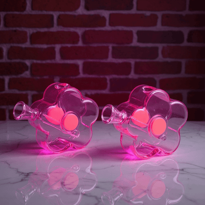 Bloom Puff Glass Bong - Cute bong for girlsBloom Puff Glass Water Pipe. Two flower - shaped clear glass pipes placed side by side on a dark wood surface