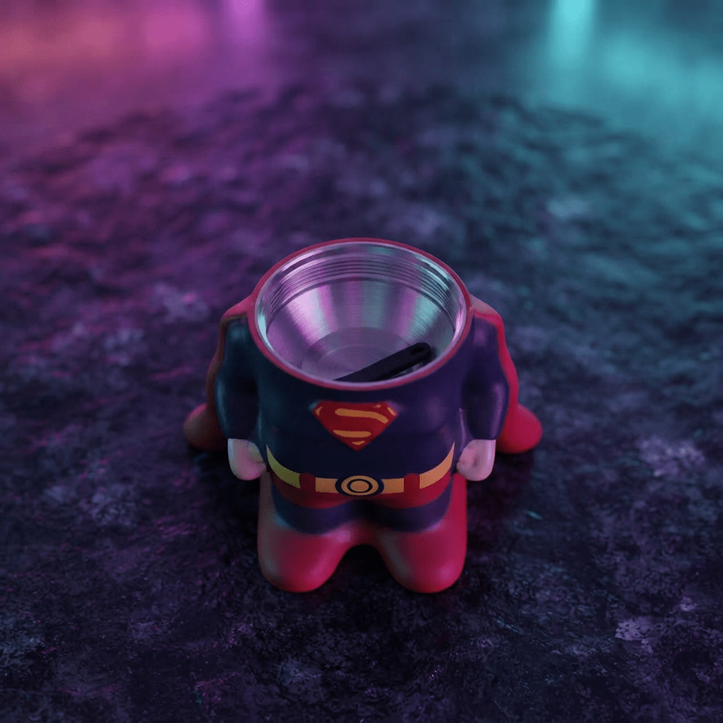 Caped Comic Hero Character Herb Grinder – Novelty Metal GrinderA Superman-themed cup or tumbler with a molded body resembling the superhero's torso, shown from above on a dark textured surface under purple and blue lighting.
