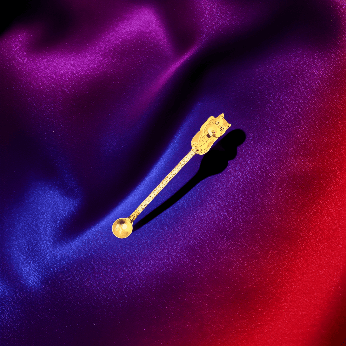 Cosmic Cat Duo Spoon SetShiny gold cat - shaped herb spoon with engraved details on a silky red and purple background.