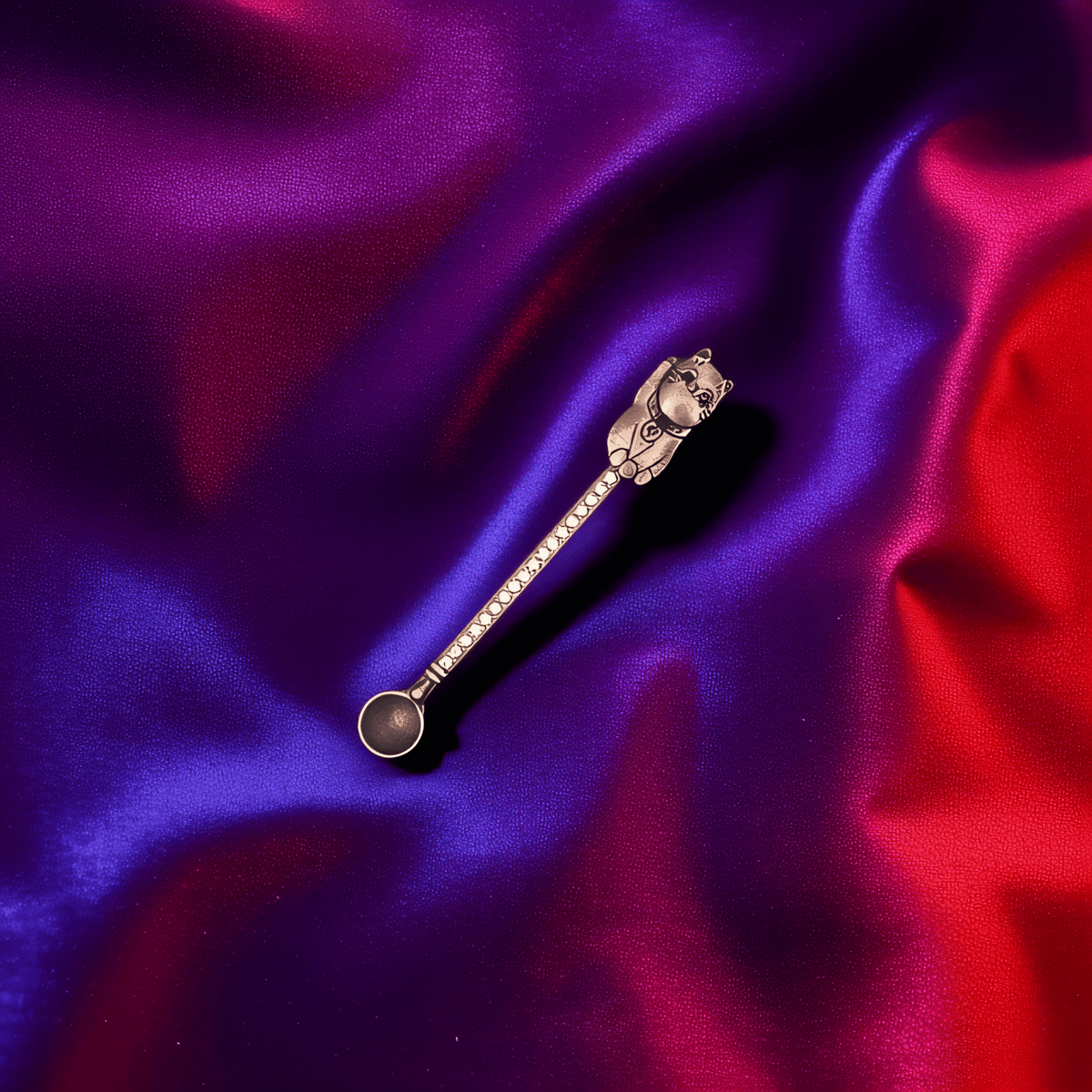Matte black cat - shaped herb spoon with mysterious charm on bold purple - red background.