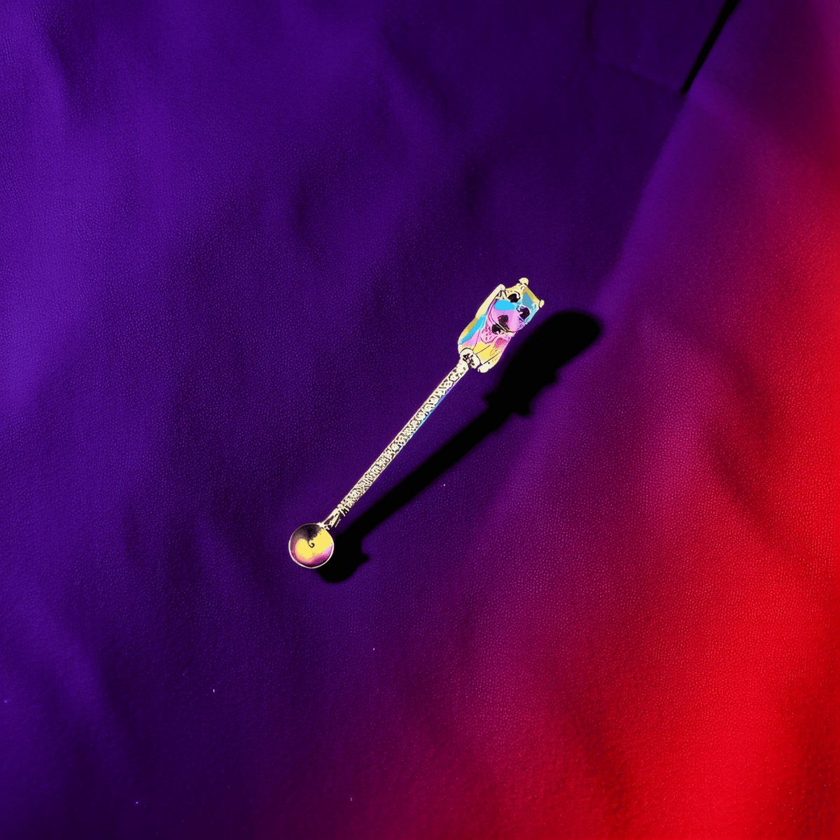 Colorful rainbow finish herb spoon shaped like a lucky cat on vibrant silk fabric.