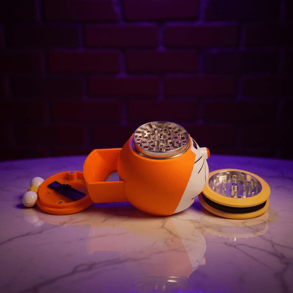 Cute Cat Crank GrinderOrange herb grinder with a metallic top on a reflective surface with a dark brick wall background.