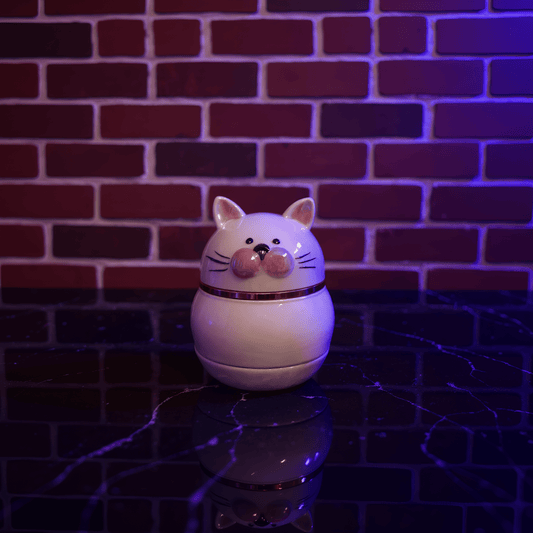 Cute Ceramic Cat Herb Grinder – Spice CrusherWhite cat - shaped herb grinder night light on a reflective surface with a brick wall background