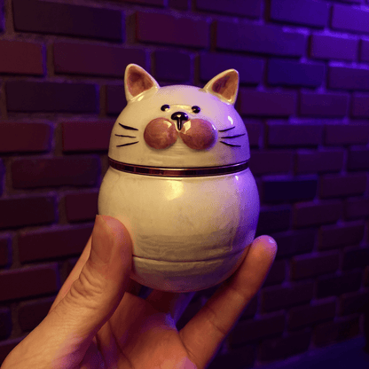 Cute Ceramic Cat Herb Grinder – Spice CrusherCeramic cat - shaped grinder held in front of a brick wall with purple lighting