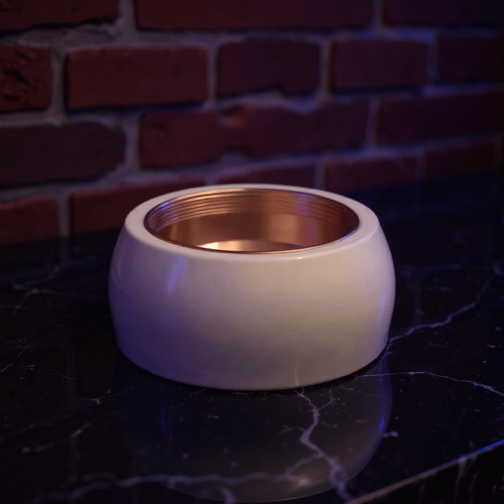 Cute Ceramic Cat Herb Grinder – Spice CrusherWhite ceramic bowl with gold interior on a dark surface against a brick wall.