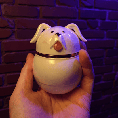 Cute Ceramic Dog Herb Grinder- Hand holding a dog - shaped ceramic herb grinder against a brick wall background