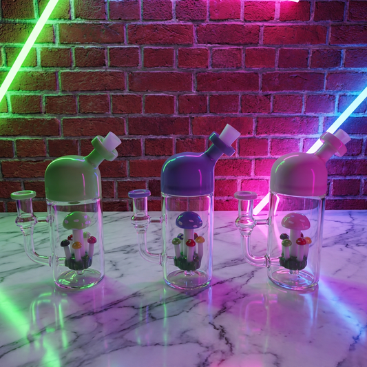 Cute Mushroom Percolator Bong – Mini Fairycore Glass BubblerClear water pipe with colorful lids on a marble surface with a brick wall background.