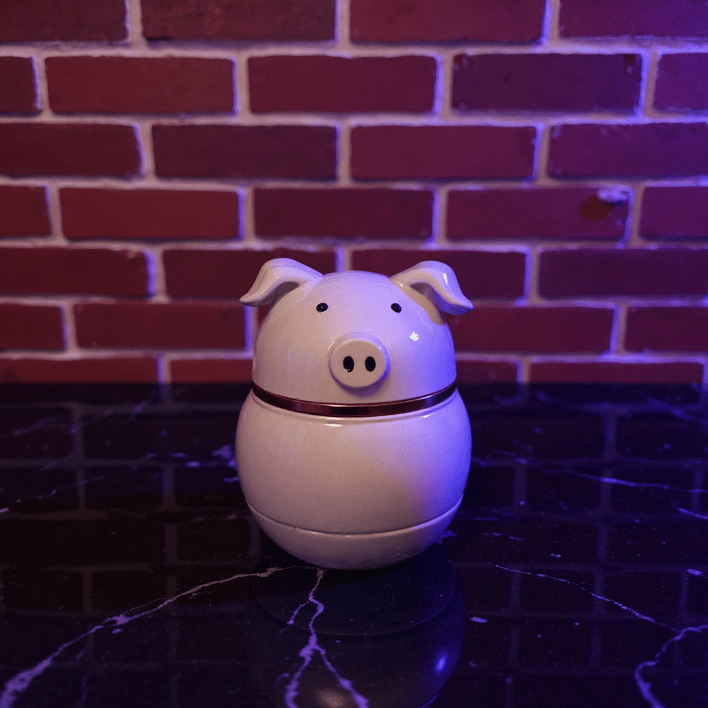 Cute Pig Ceramic Herb Grinder – Spice Crusher- White pig shaped ceramic grinder on a dark surface with a brick wall