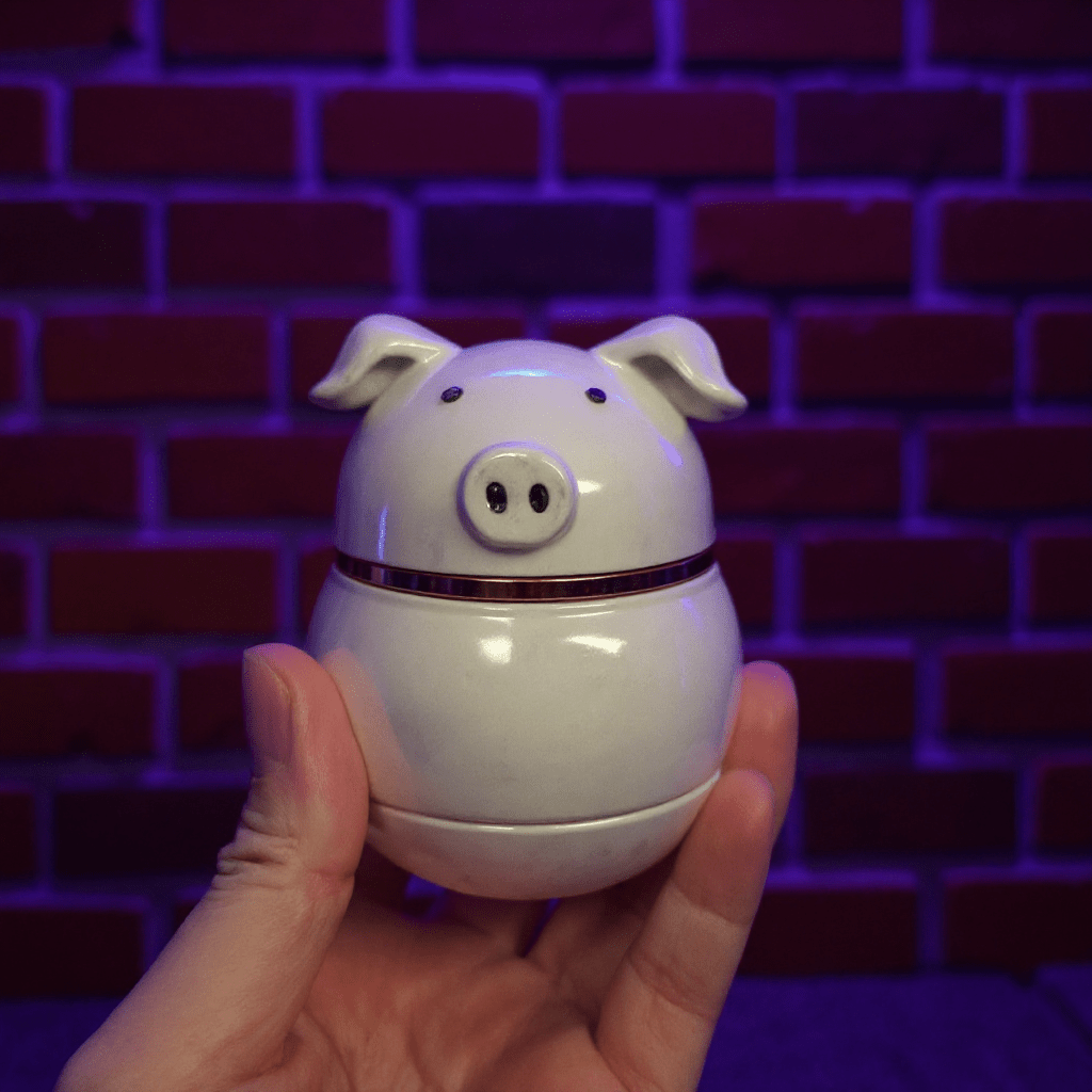 Cute Pig Ceramic Herb Grinder – Spice Crusher- White pig shaped ceramic herb grinder held in front of a brick wall