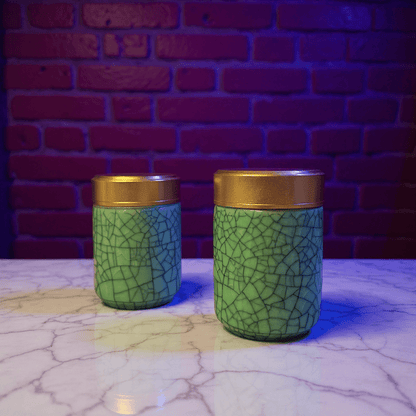 Deep Green Celadon Porcelain Stash Jar – Large & Small SizesTwo green ceramic jars with gold lids on a textured surface