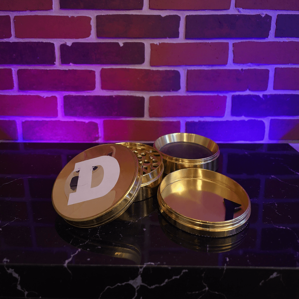 Doge Meme Herb Grinder - Gold - colored grinder with a doge logo on a dark surface against a brick wall with purple lighting