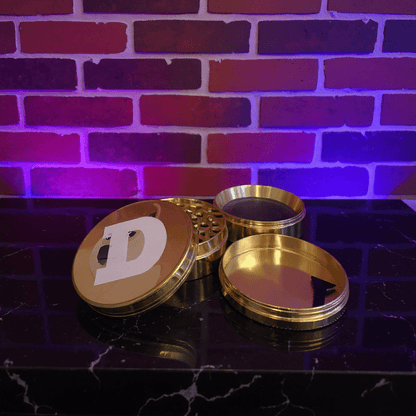 Doge Meme Herb Grinder - Gold - colored grinder with a doge logo on a dark surface against a brick wall with purple lighting