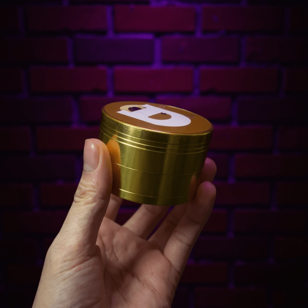 Doge Meme Herb Grinder - Gold - colored grinder with a logo held in a hand against a brick wall background
