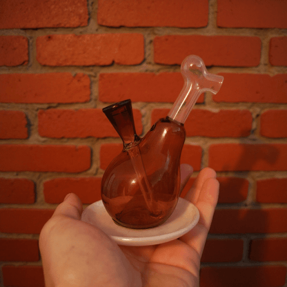 Drumstick Glass Bong – Mini Turkey Leg Water Pipe - Hand holding a small glass water pipe against a brick wall background