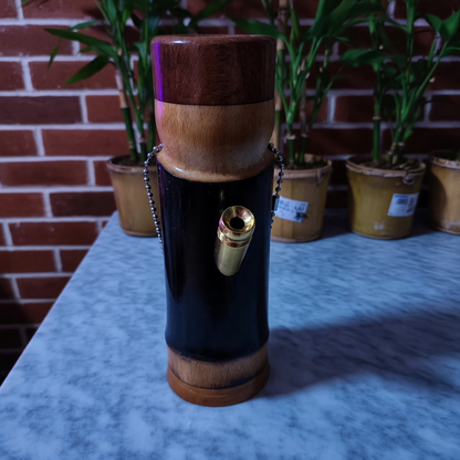 Bamboo bong with a gold accent on a marble surface, with plants and a brick wall in the background.