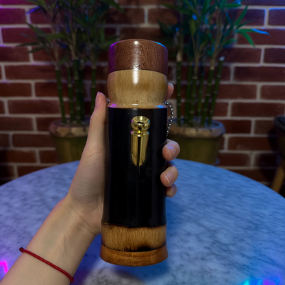 Hand holding bamboo bong with a gold accent against a brick wall.