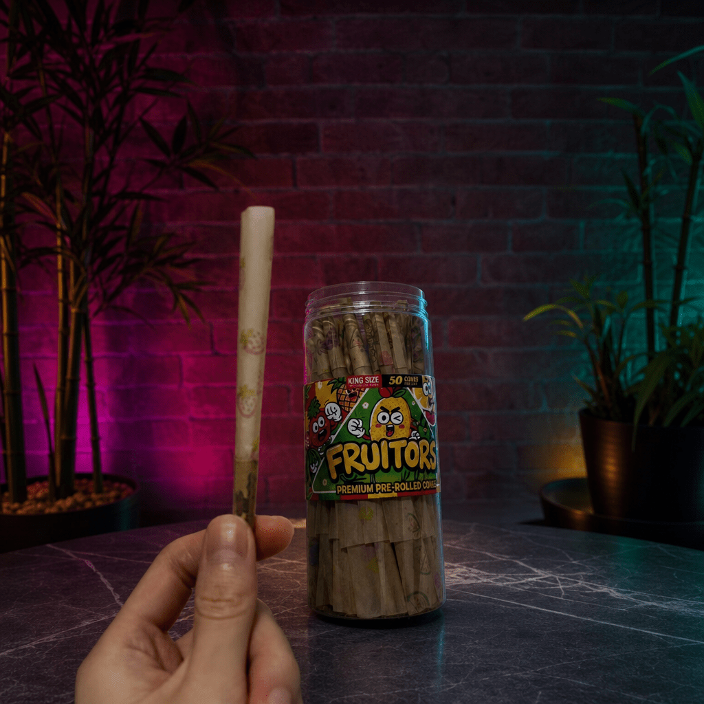 FruitBurst King Size Fruit Flavored Pre - Rolled Cones – 50 PackHand holding a pre - rolled joint next to a container of Fruitors pre - rolled joints with a dark background.