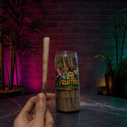FruitBurst King Size Fruit Flavored Pre - Rolled Cones – 50 PackHand holding a pre - rolled joint next to a container of Fruitors pre - rolled joints with a dark background.
